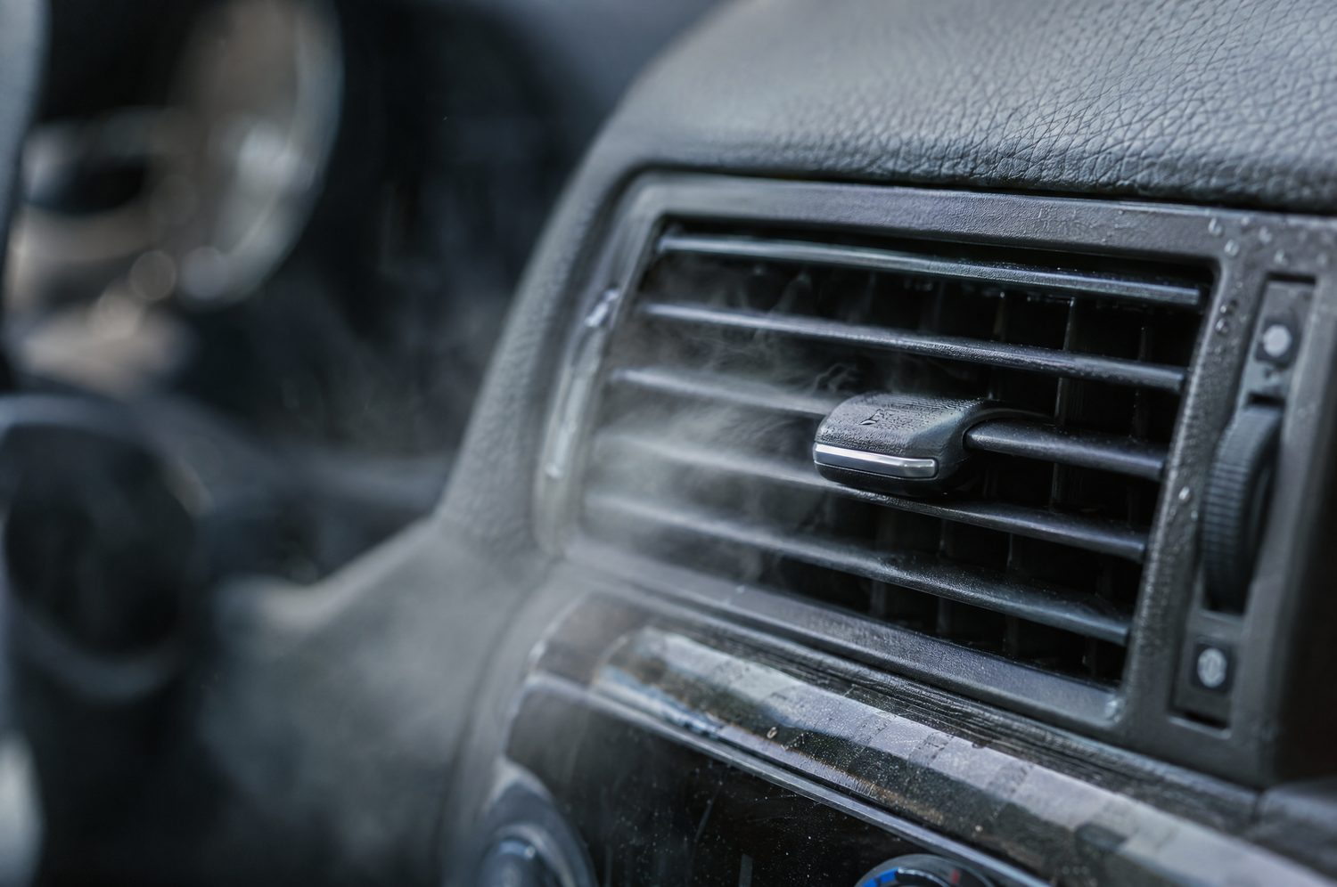 Close-up van een ventilatierooster in het dashboard van een auto waaruit lucht blaast, met lichte condens