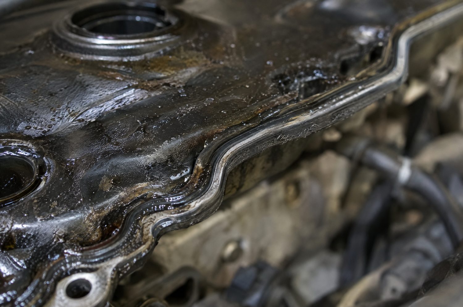 Close-up van de rand van een kleppendekselpakking op een automotor, bedekt met olie en vuil