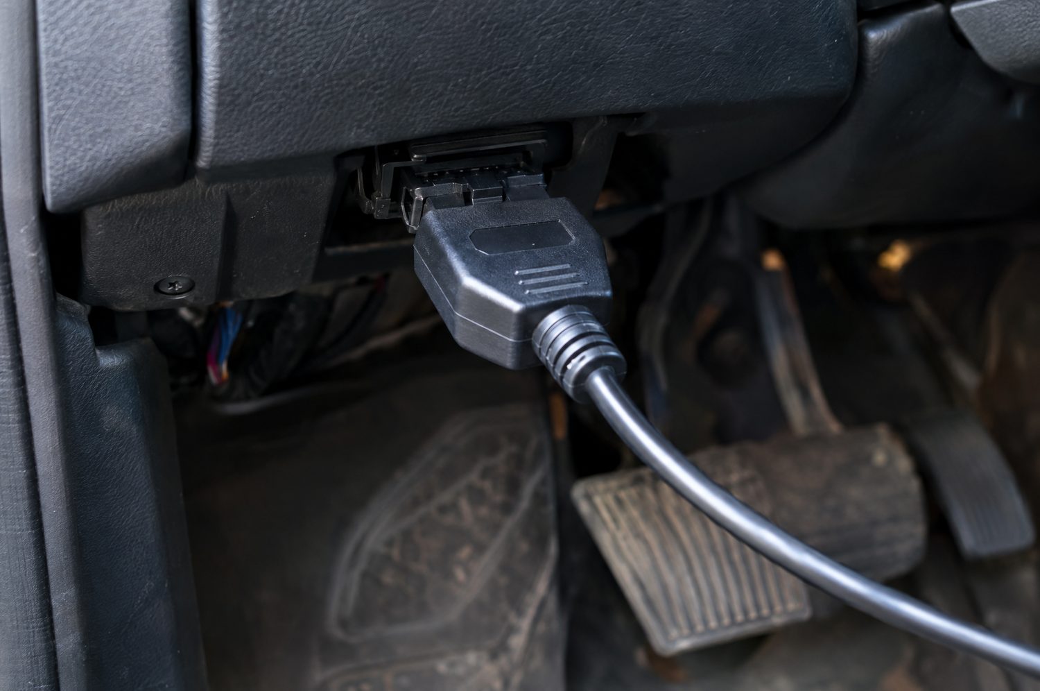 OBD-II-diagnosestekker onder het dashboard van een auto met een aangesloten diagnose-interface en een kabel die wegloopt