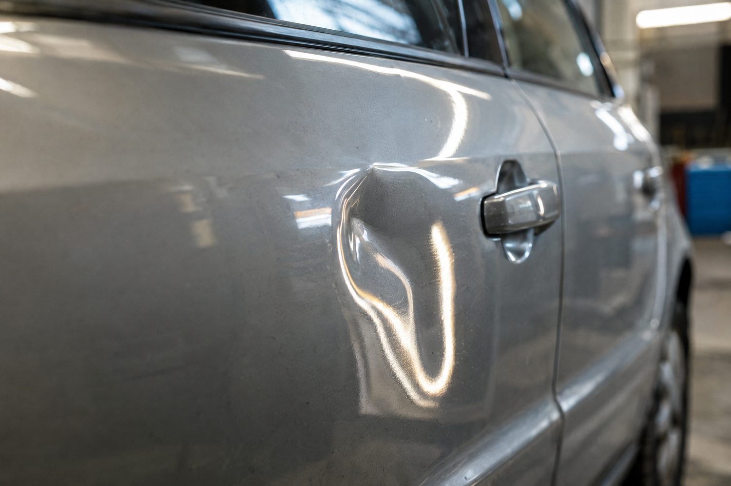 Close-up van een kleine deuk in een zilveren autodeur, met gereflecteerde lichtlijnen die rond de deuk vervormd zijn
