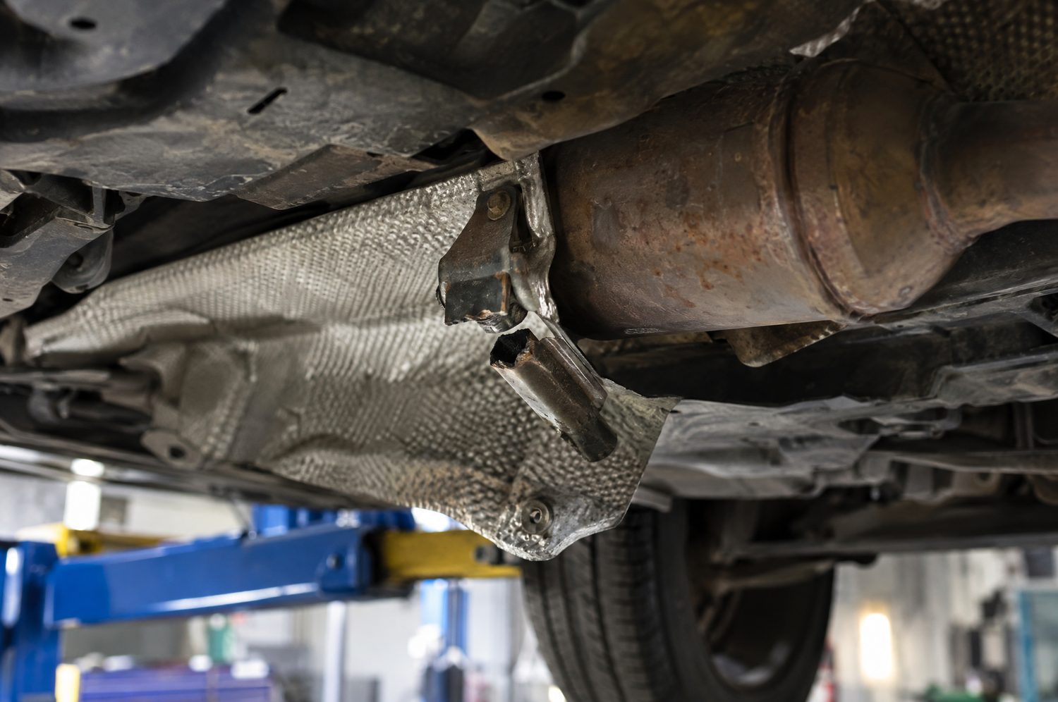 Los hitteschild van de uitlaat met een afgebroken beugel, gezien vanaf de onderkant van een auto op de brug